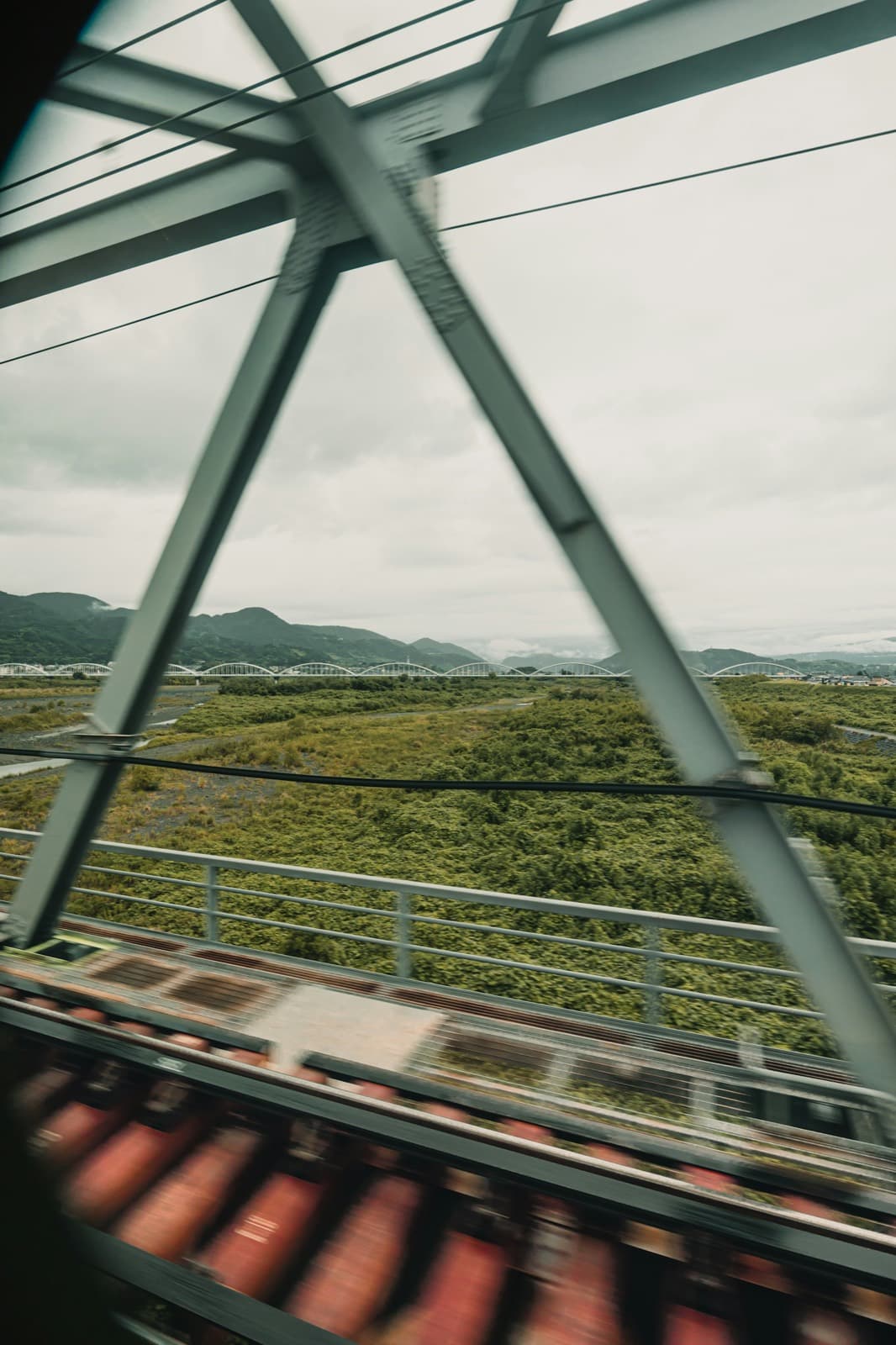 A view from a train crossing a steel bridge over a green river valley