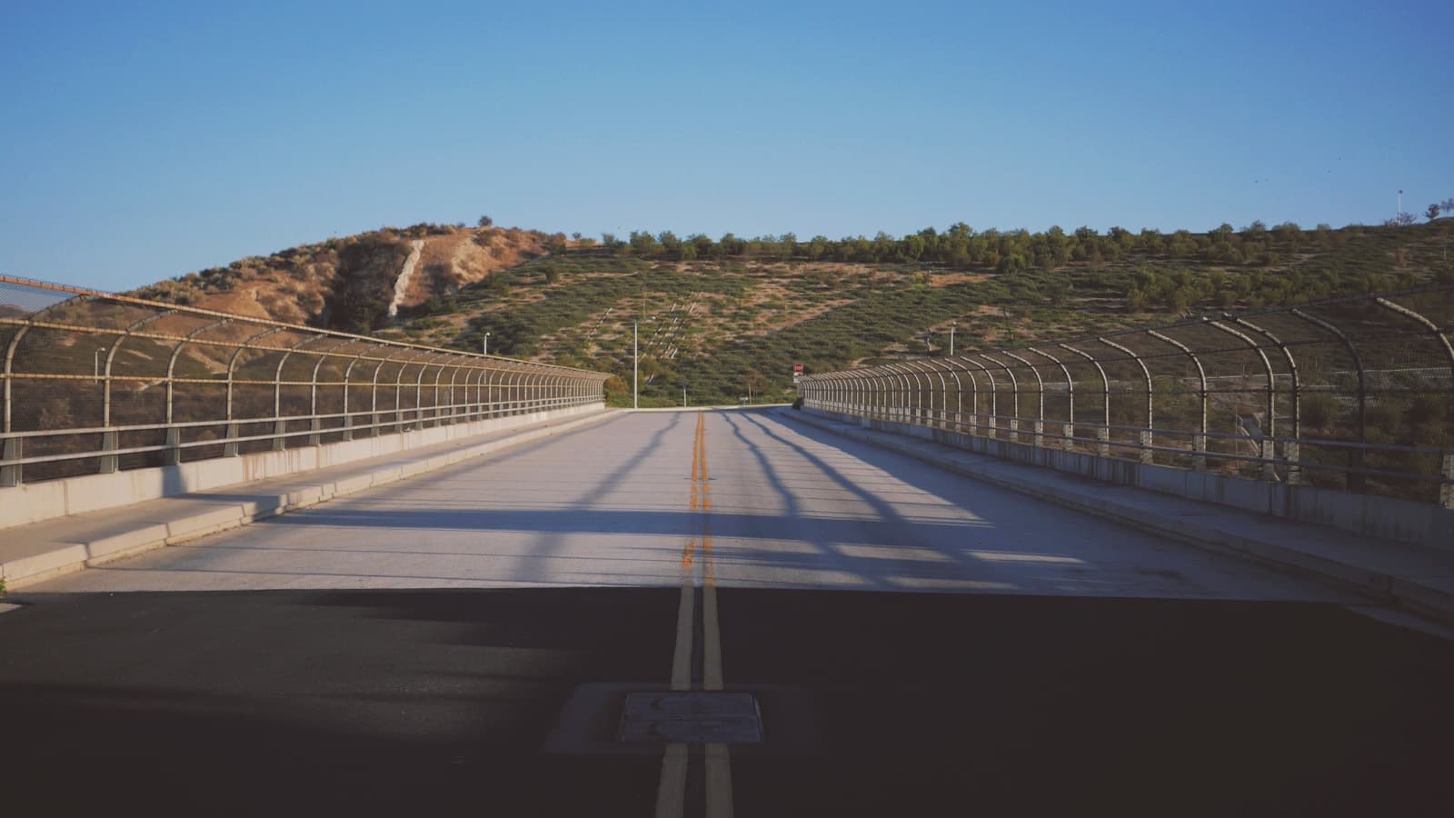 An empty road bridge with railings leading towards a hillside